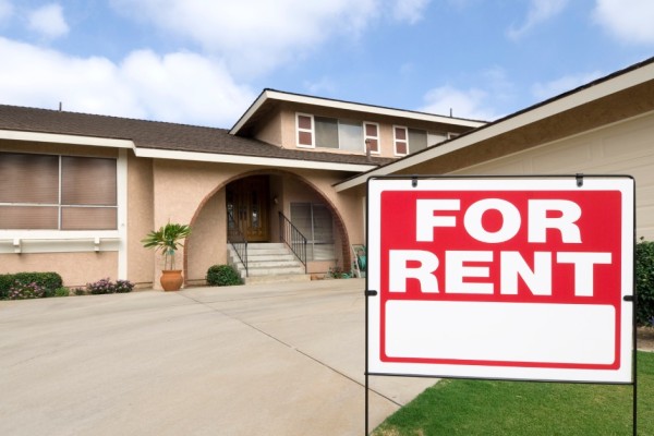 A bright red "For Rent" sign posted outside of a single-story, single-family home with a minimalist vibe.