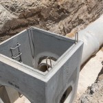 A concrete sewer line mid-construction surrounded by rubble and torn-apart street. The pipeline is in a residential area.