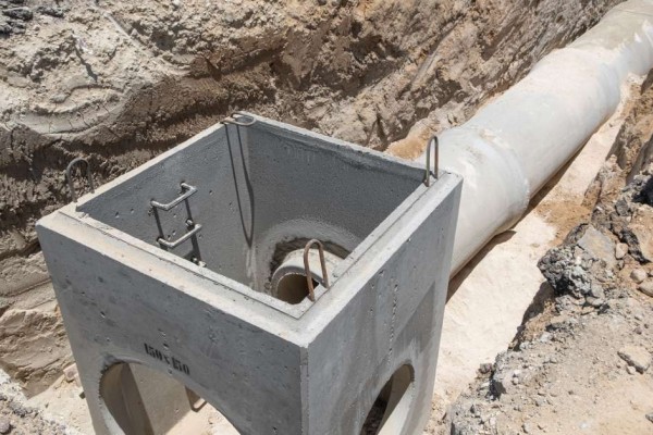 A concrete sewer line mid-construction surrounded by rubble and torn-apart street. The pipeline is in a residential area.