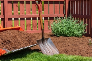 A red-orange machine has a bucket attachment filled with brown mulch on the front. A shovel is in front of the bucket.