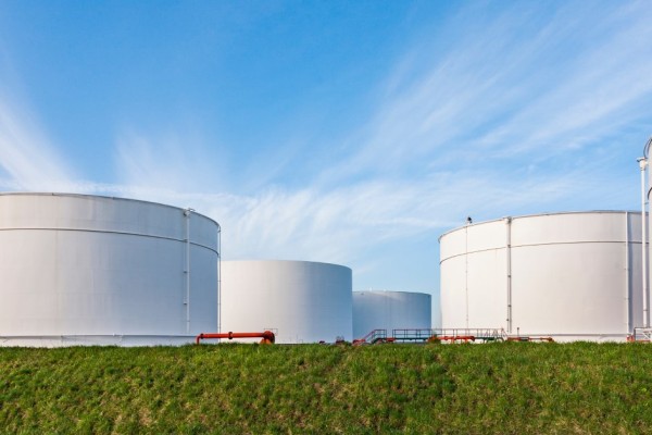 Five large, white storage tanks sit in the middle of a grassy area. The blue sky appears in the background.