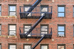 The exterior of a multi-story red brick building with several windows and a black metal fire escape.