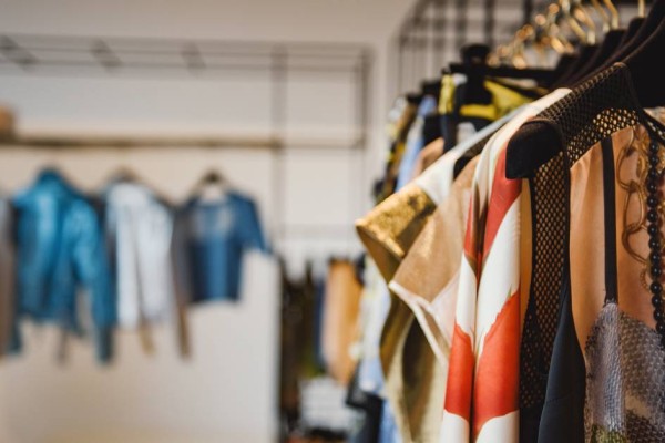 Several patterned tops hanging off black clothing hangers on a black bar, with blurry clothes hanging in the background.