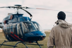 A helicopter pilot in a tan hooded flight suit and toque is seen from behind as he approaches his helicopter.