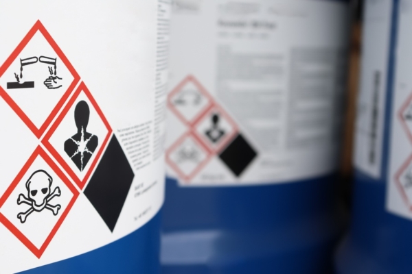 A close-up of three blue chemical tanks with various hazard warning symbols on the sides of their labels.