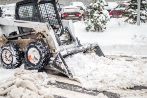 A compact tractor using a front-mounted snow bucket attachment to clear snow in a commercial parking lot.