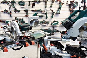 An assortment of power saws and other electrical tools are displayed on a table and hanging from pegs on a wall.