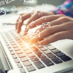 A close-up view shows a person typing on a laptop. There are small, white-outlined envelopes floating from the keyboard.