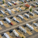 Aerial view of a large RV park with multiple parking rows with white RVs, driving lanes, and scattered small trees.