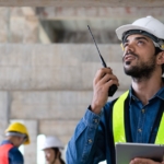 A property developer manager is using a walkie-talkie to communicate safety policy with workers on site.