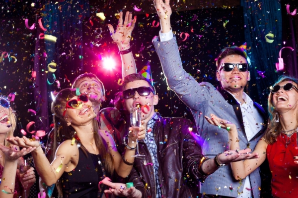 Young adults standing together in formal attire, smiling and wearing sunglasses, and celebrating under falling confetti.