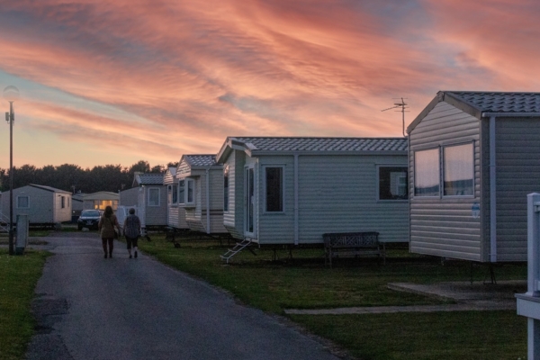The sun sets over a group of mobile homes in a mobile home park. The clouds are a gorgeous shade of orange and purple.