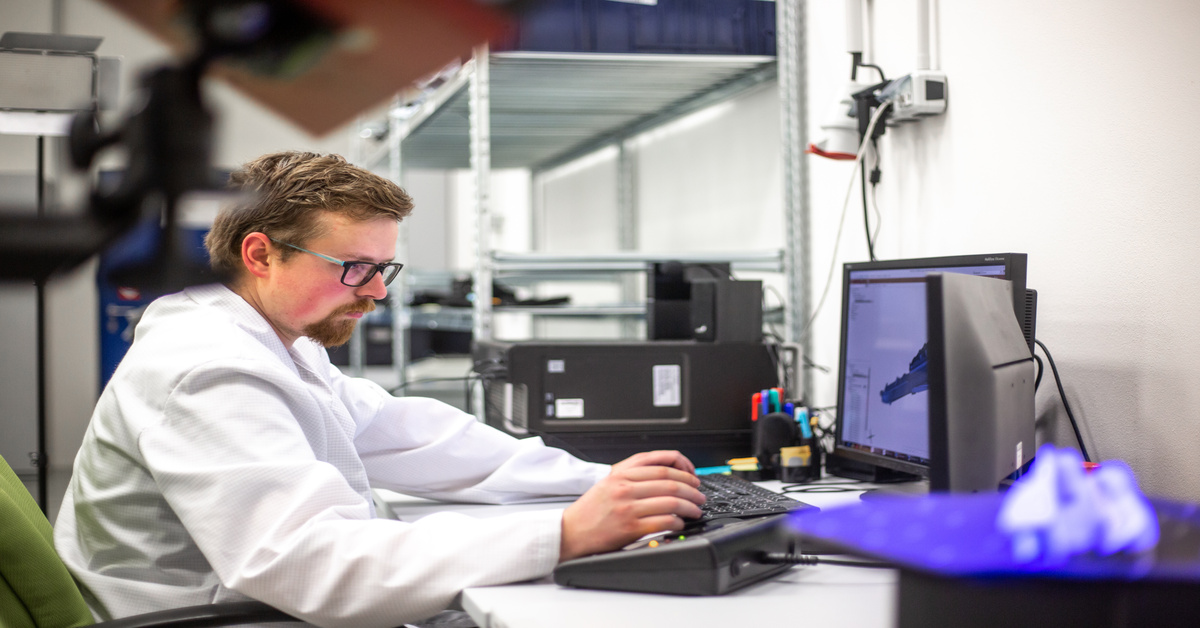 A man working at a computer on a 3D object. In the foreground, there is an object getting scanned by a 3D scanner.