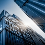 Several shipping containers are stacked on top of each other. The containers are blue and one has white labeling on it.