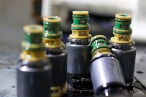 A close-up view shows a group of five solenoid valves sitting on a dark-colored surface. The background is blurry.