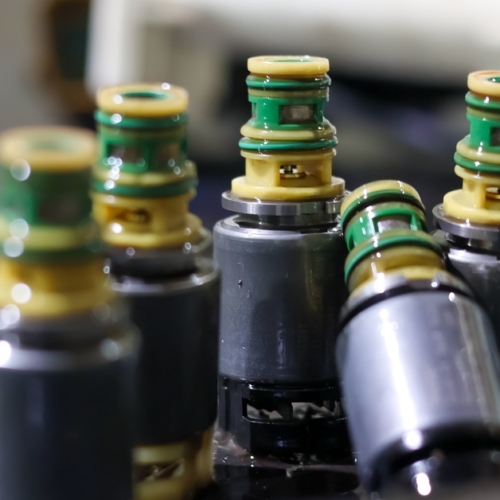 A close-up view shows a group of five solenoid valves sitting on a dark-colored surface. The background is blurry.