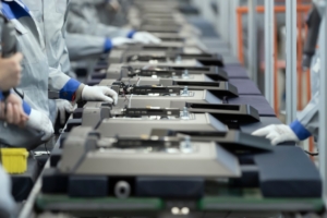 A group of employees working on a production line. The conveyor belt in front of them is full of large metal devices.