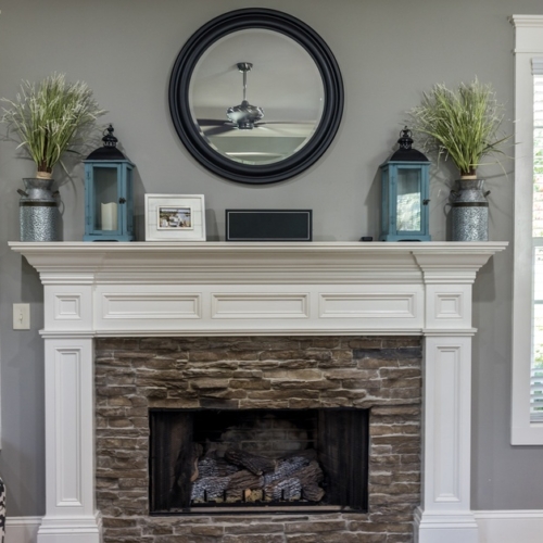 A gas fireplace area with a white mantle over the top. The mantle has decorative lanterns and a mirror hanging on the wall.